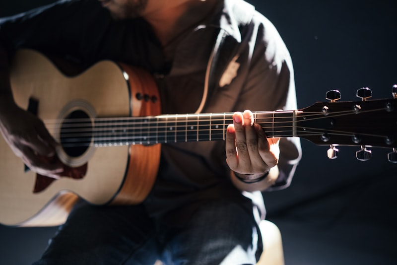 A person practicing acoustic guitar while sitting on a wooden floor.